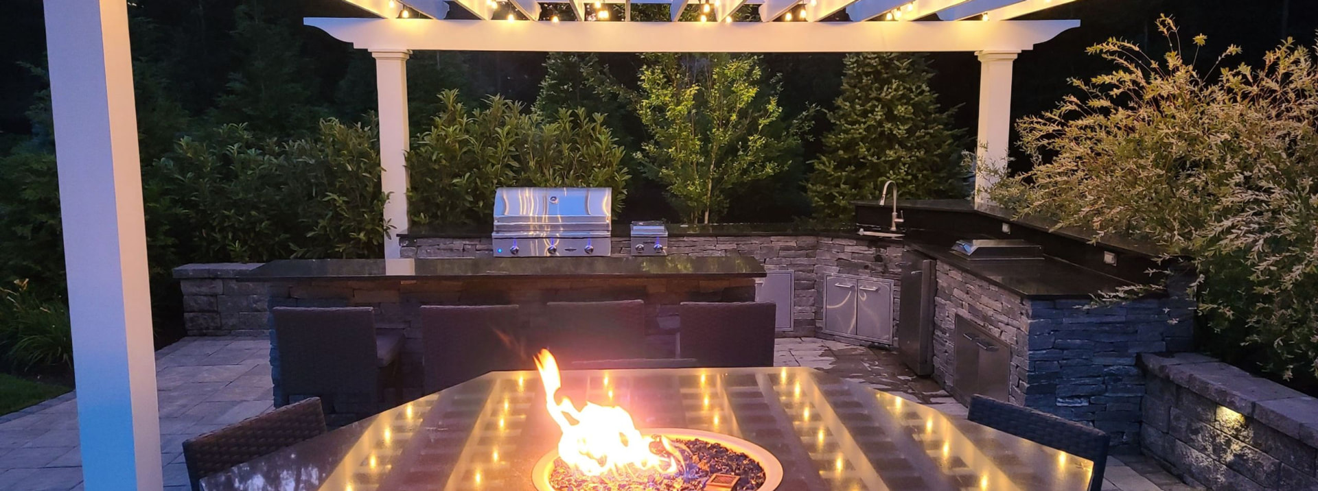 Completed outdoor kitchen and fire feature under a beautifully lit pergola