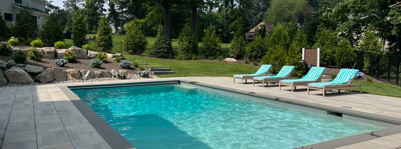 Inground pool with a paver patio, lounge chairs and natural boulder plantings
